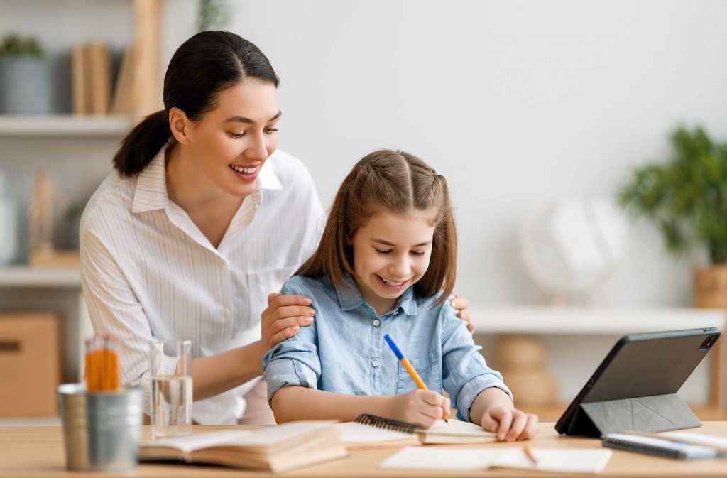 Back to school. Happy child and adult are sitting at desk. Girl doing homework or online education.